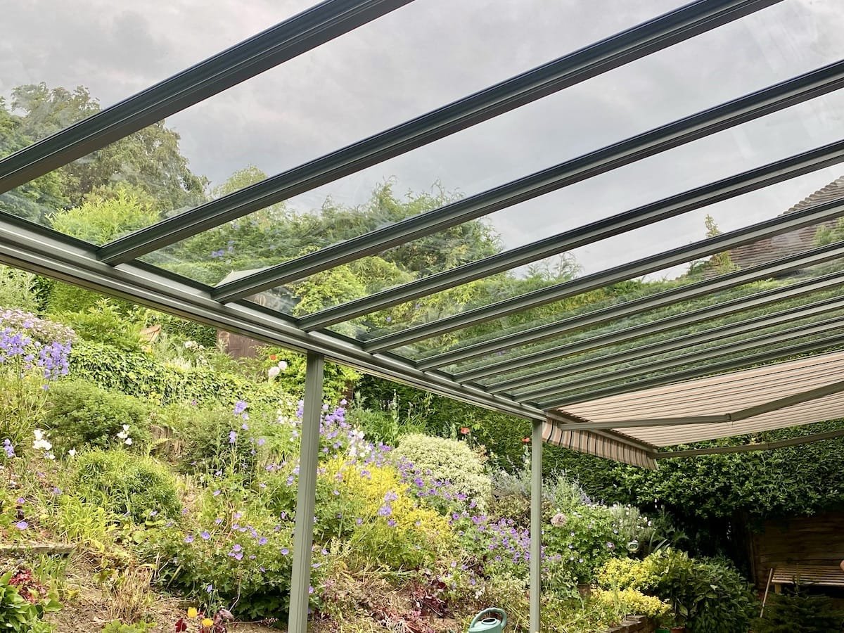 Glass-roofed patio structure over a colorful garden with purple and yellow flowers and green shrubs
